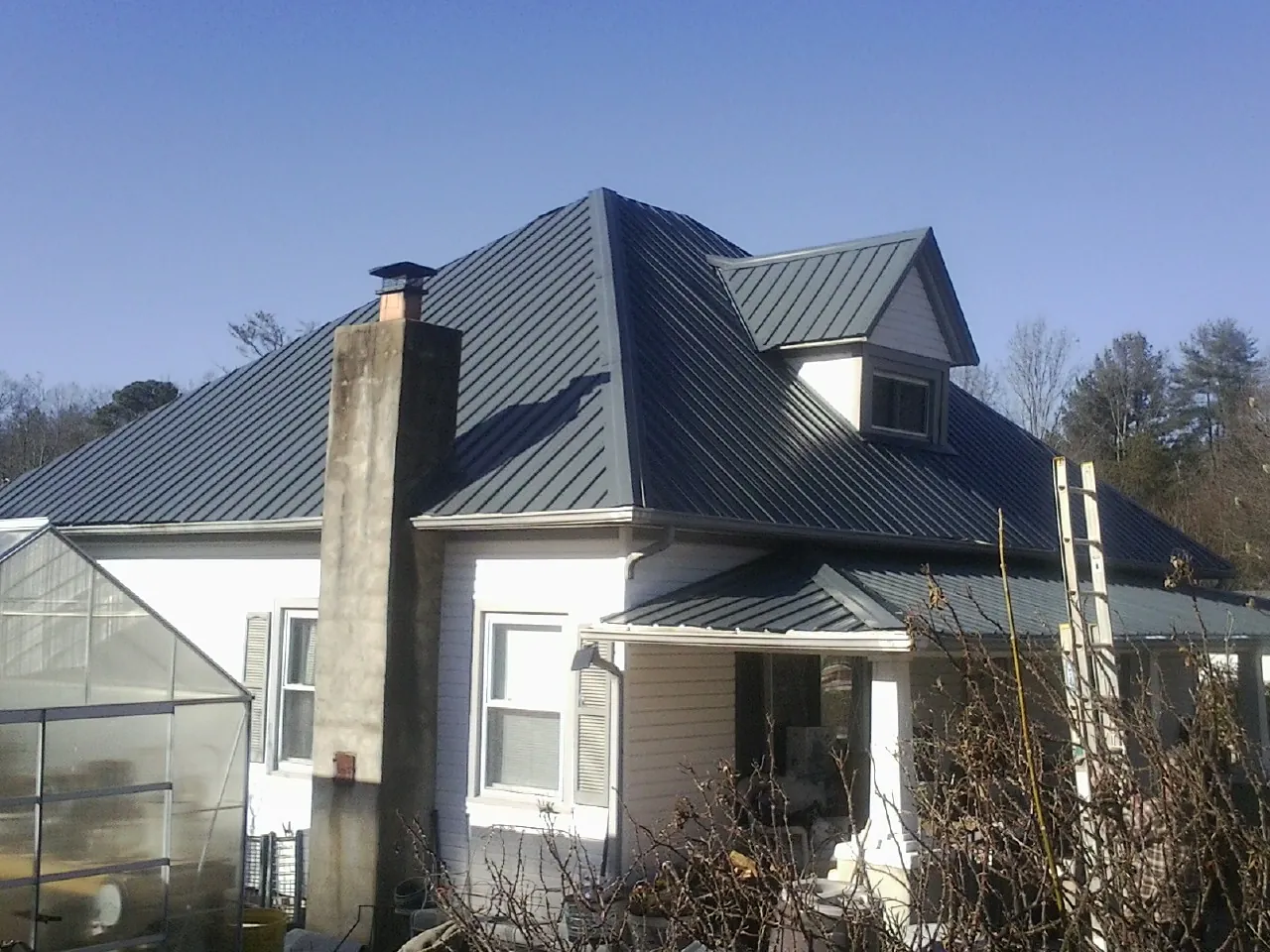 Dark blue standing seam metal roof on a white farmhouse with dormer — Slate & Tile Roof Repair by Roofing Brothers in Volcano