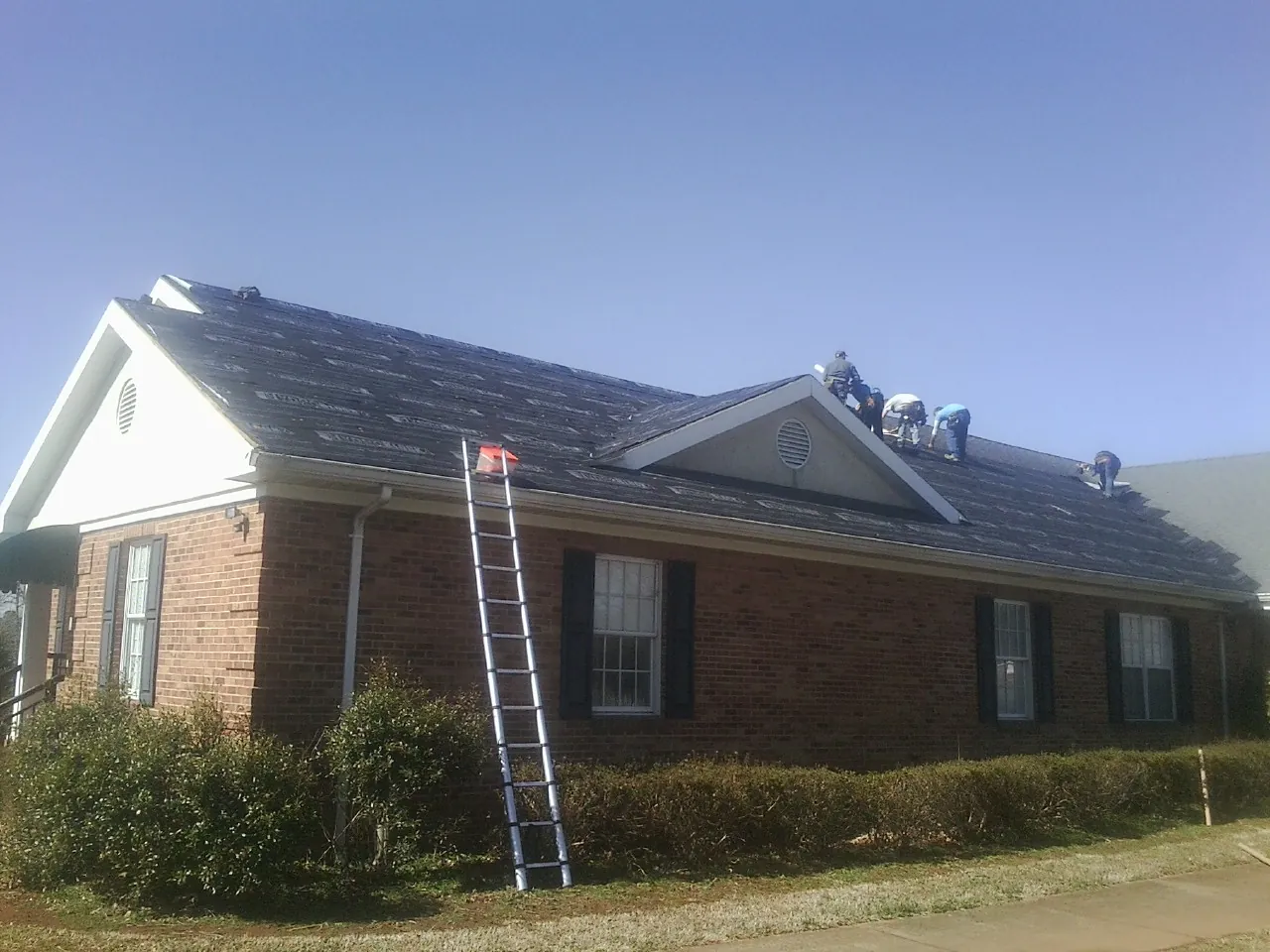 Crew tearing shingles off a brick ranch roof with a ladder set — Emergency Roof Repair work by our crew in Volcano