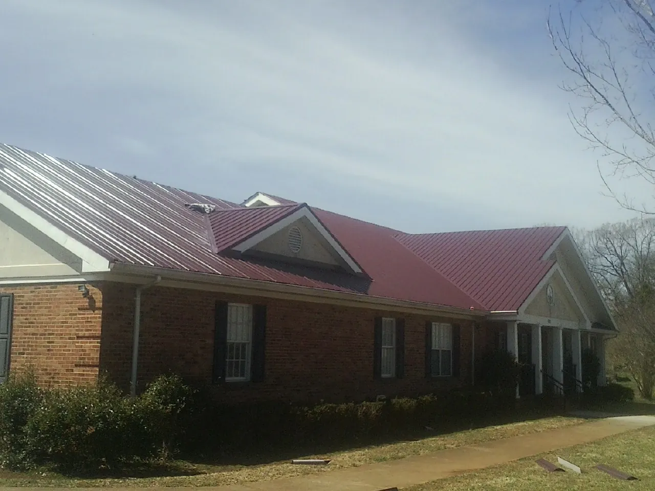 Red metal roof with gabled entries on a long brick building, from a Hail Damage Roof Repair job in Volcano