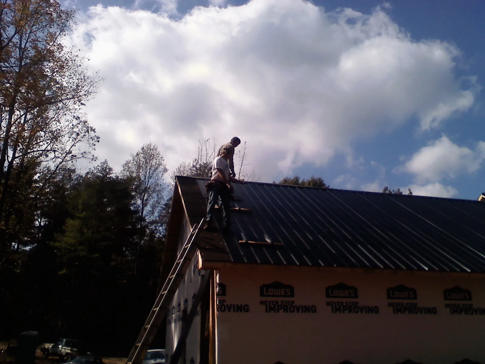Roofer fastening dark metal panels high against a cloudy sky, from a Roof Inspection job in Volcano