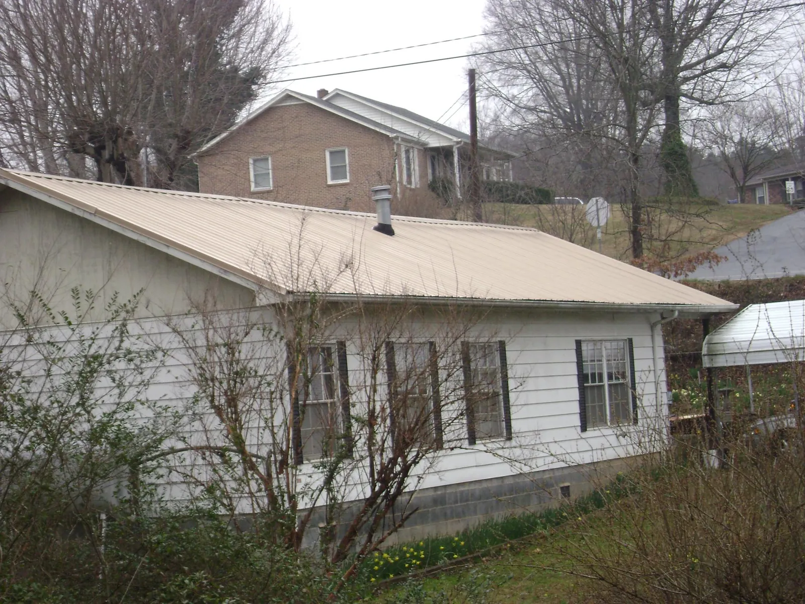 Tan metal roof on a white sided house set into a hillside — Commercial Roofing by Roofing Brothers in Volcano