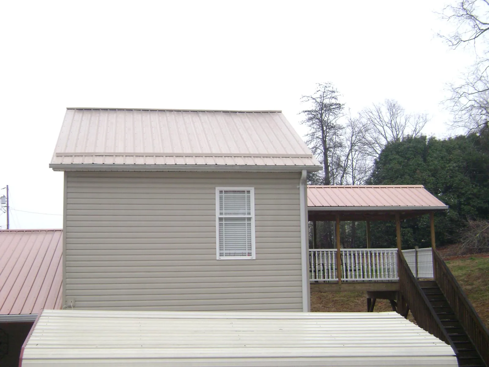 Tan metal roofs on a two story addition and attached porch, from a Roof Replacement job in Volcano
